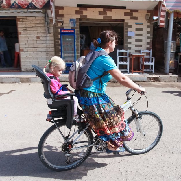 Maman dans la rue avec sa fille sur le porte bébé pour vélo