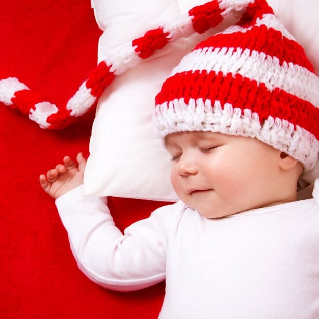 bébé qui dors avec un bonnet rouge et blanc sur un oreiller