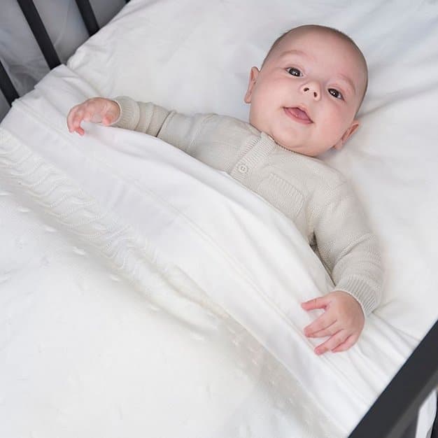 bébé regardant la caméra sur son lit avec sa couverture avant de dormir