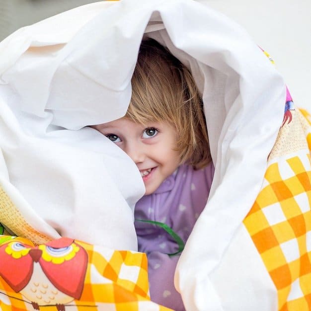 bébé se cache dans sa couverture préférée en jetant un regard dehors en souriant