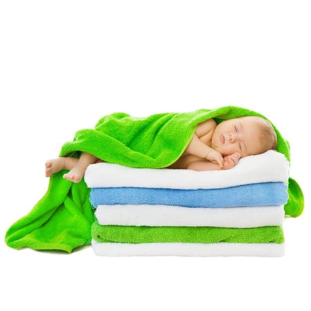 bébé qui dort sur cinq serviettes pliées et couvert d'une verte