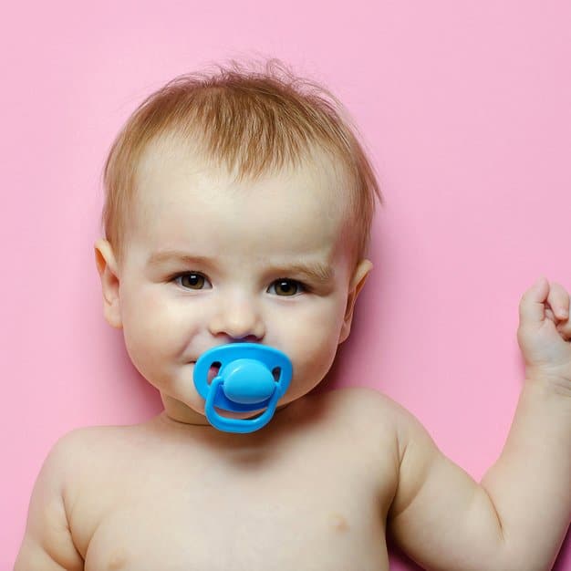 petit bébé avec une tétine bleue sur fond rose