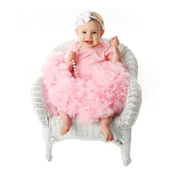 bébé souriant en robe rose assit sur un transat blanc