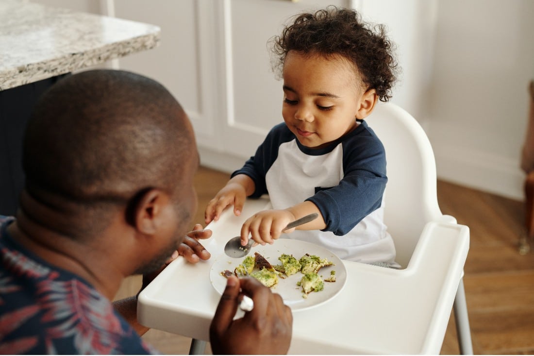 un papà che dà da mangiare verdure al suo bambino