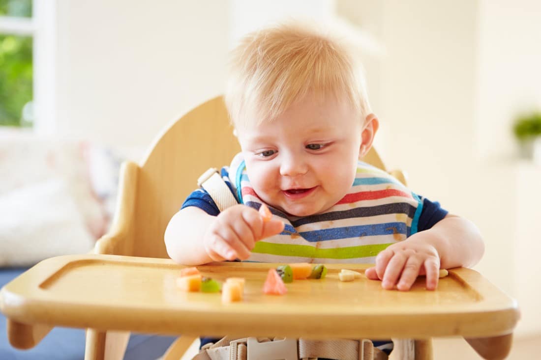 un bambino seduto nel suo seggiolone che mangia frutta tagliata in piccoli pezzi