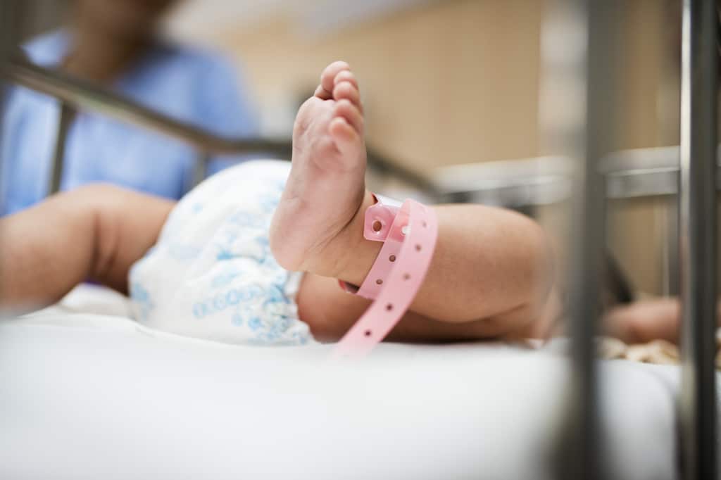 un bambino giace nella sua culla in ospedale con una vista delle sue gambe e il braccialetto avvolto intorno alla sua caviglia