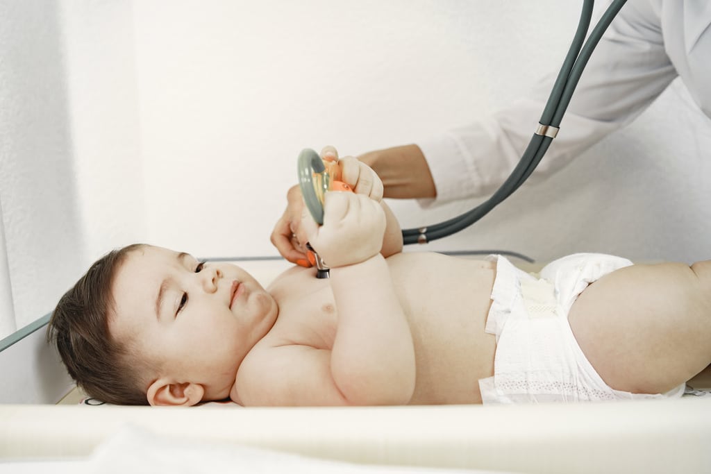 un bambino sdraiato nello studio del pediatra tiene un giocattolo tra le mani mentre il pediatra gli mette lo stetoscopio sul petto
