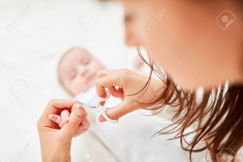 un bambino sdraiato ha la mano tesa tenuta dalla madre che gli sta tagliando le unghie con una forbice a punta rotonda