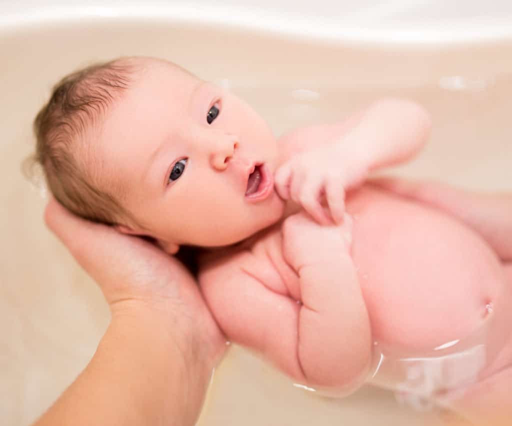 il modo migliore per fare il bagno al bambino è nella sua vasca da bagno. con la bocca aperta e le braccia contro il petto. con una mano adulta che gli tiene la testa e il collo