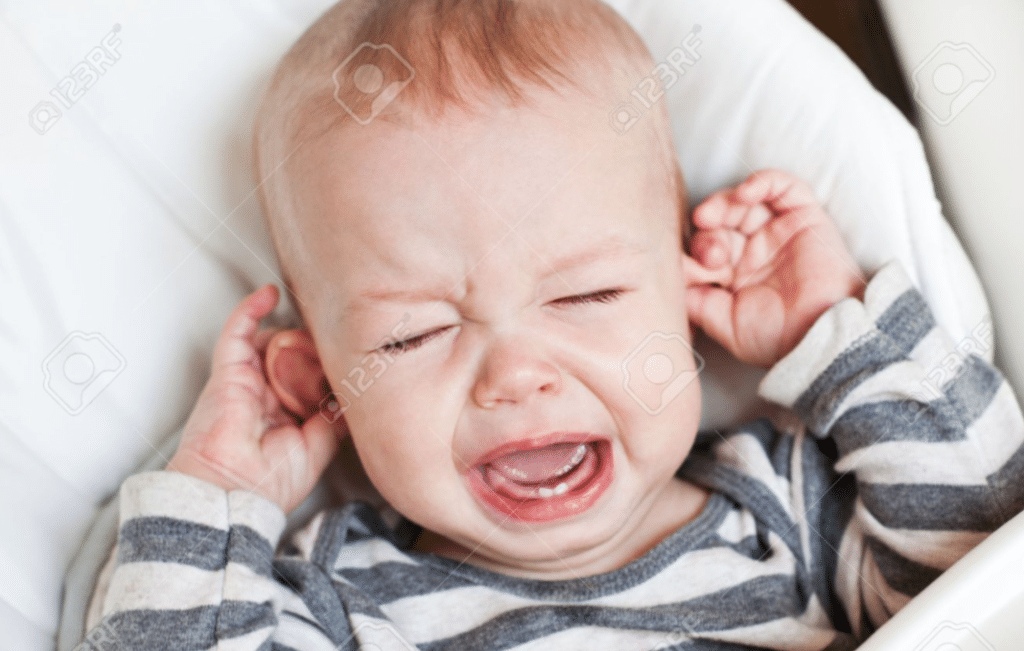 un bambino sta urlando nella sua culla e spalanca la bocca, gli occhi chiusi e si tocca le orecchie