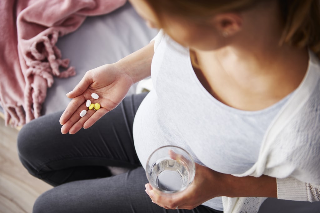 una donna incinta tiene delle pillole in mano e un bicchiere d'acqua nell'altra