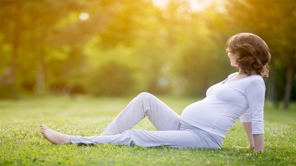 una donna incinta di 5 mesi, vestita di bianco, riposa nell'erba di un parco alberato