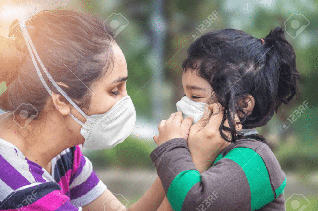 una bambina e sua madre sono di profilo e indossano una maschera ffp2. la madre sta regolando la maschera sul viso della figlia.