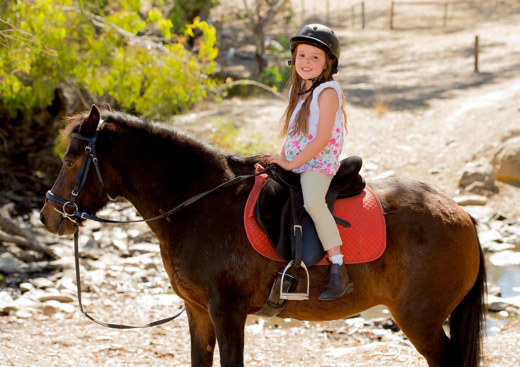 una bambina è su un pony con il suo casco di sicurezza addosso, pronta a fare un giro