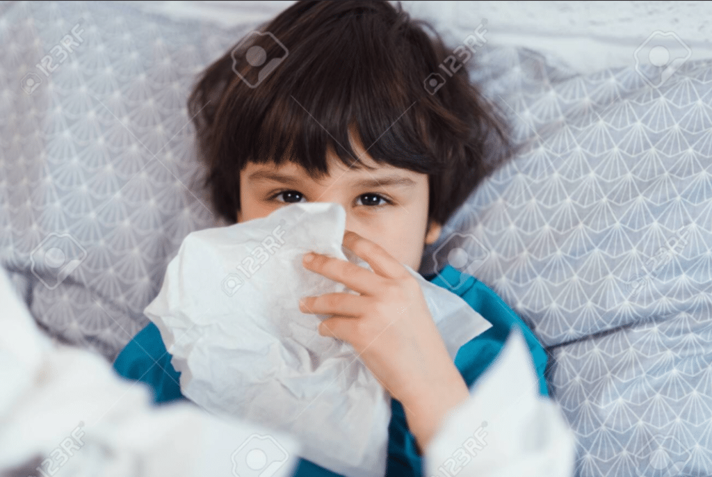 Raffreddore omeopatico per bambini: un bambino con un fazzoletto che copre parte del suo viso giace a letto.